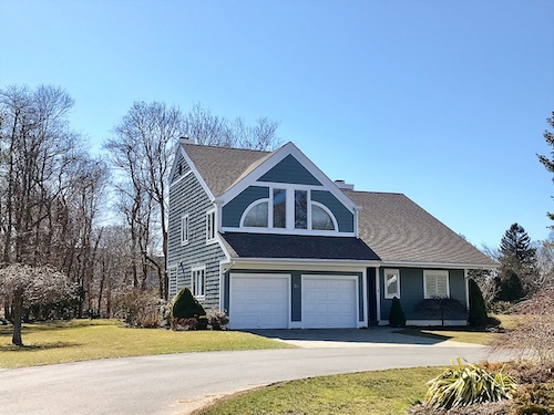 Suburban house with blue siding, large arched window, dual garage doors, and a sloping roof.