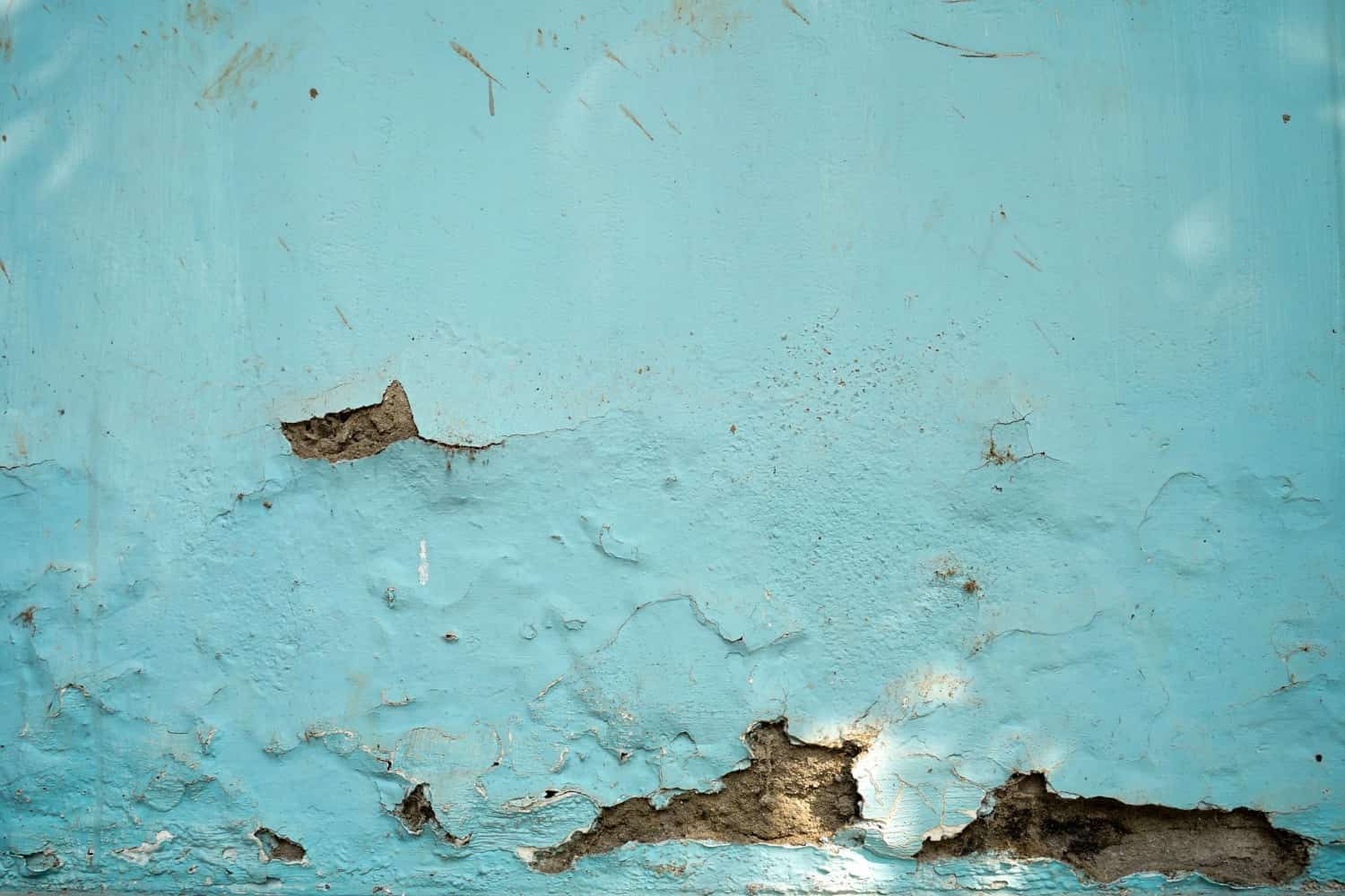 Peeling light blue paint reveals cracked plaster on an aged wall.
