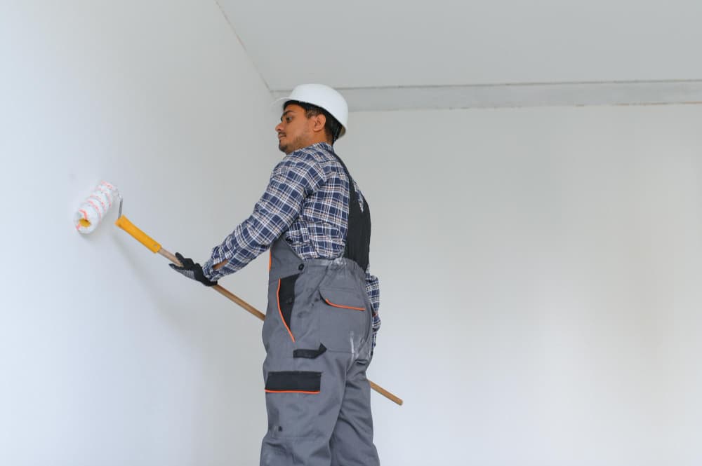 Professional painter applying white paint to an interior wall with a paint roller.