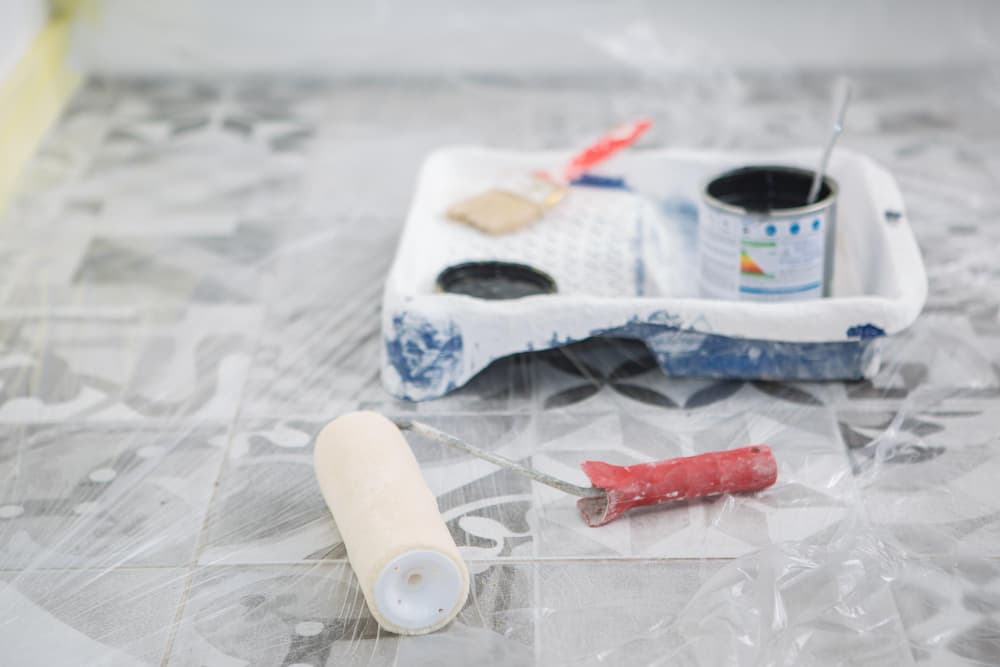 Paint roller and tray on covered tile floor during home renovation.