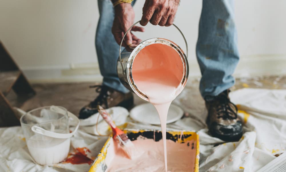 Contractor pouring light-colored paint into a tray during an interior painting project.