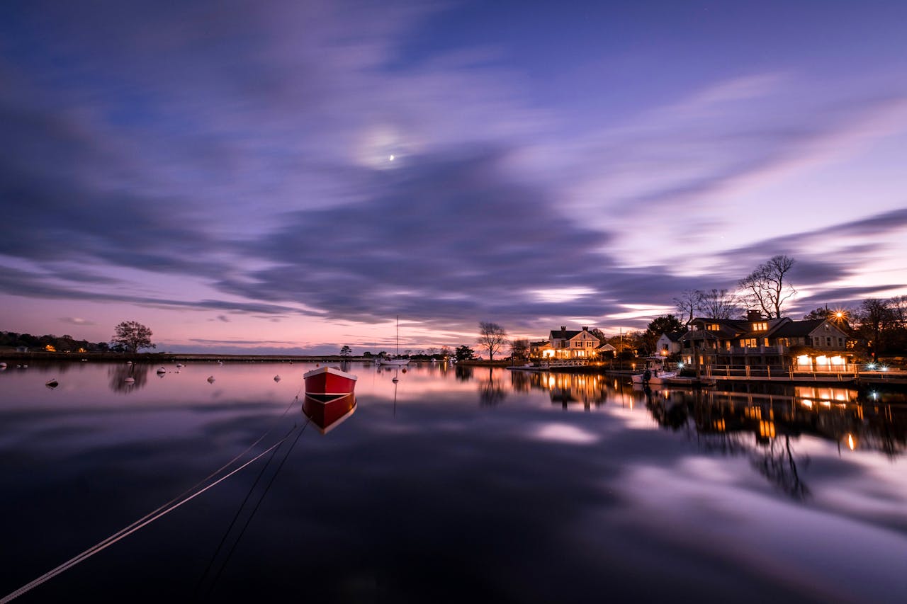 Calm twilight scene of a red boat on still water reflecting the evening sky in Fairfield, CT