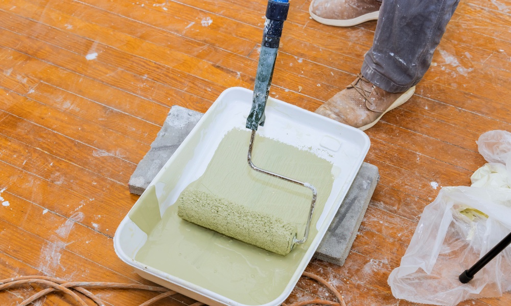 paint roller being dipped into a tray of sage green paint