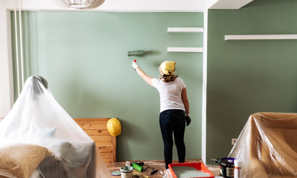 A woman using a roller to paint an interior wall