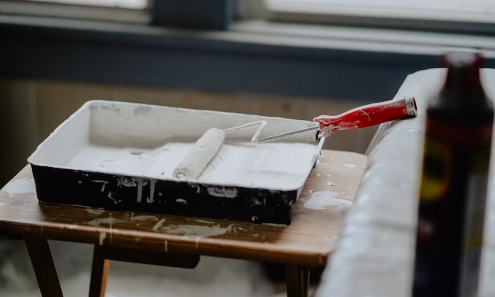 A paint roller with white paint resting in a plastic tray