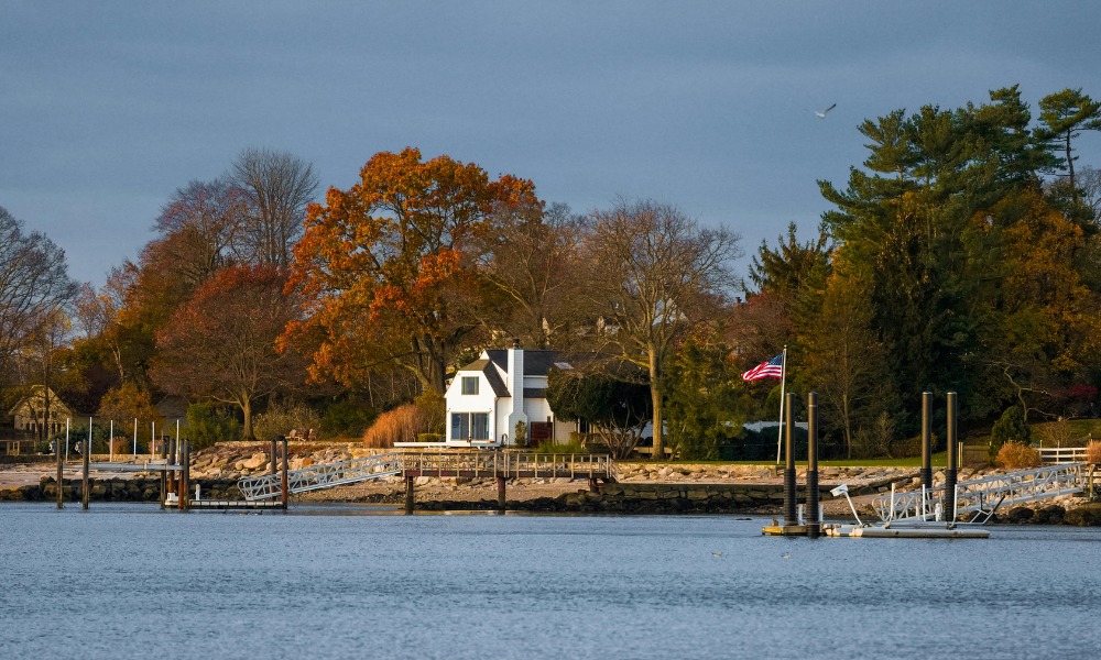 A white waterfront house with private docks surrounded by colorful autumn trees