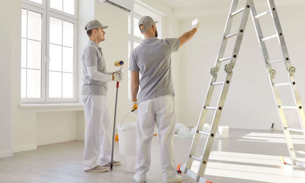 two painters in grey shirts and caps discussing wall details