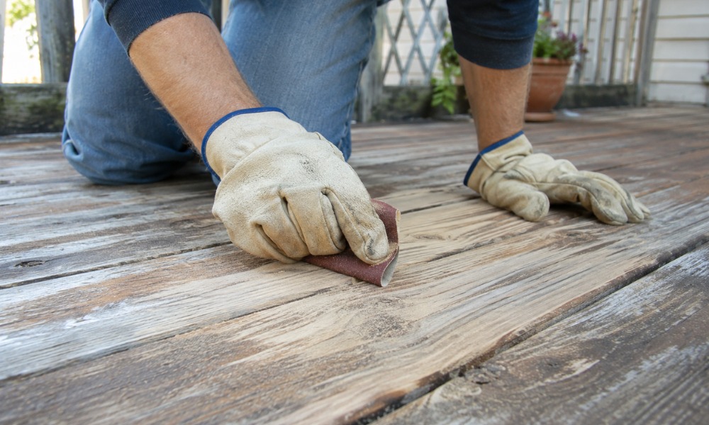 Worker in leather gloves using sandpaper to smooth a weathered wooden deck