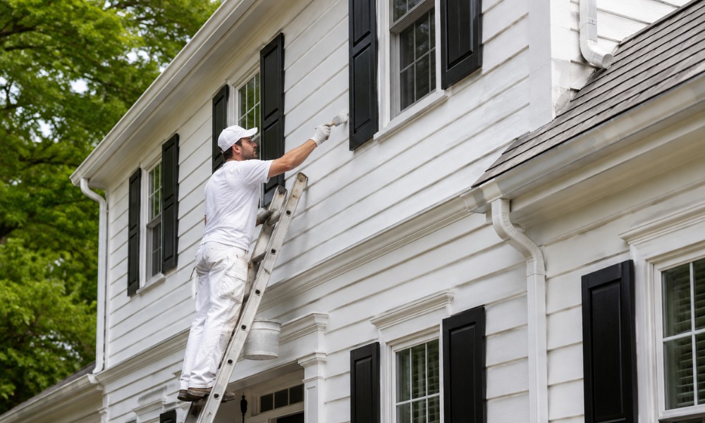professional painter on a ladder applying white exterior paint