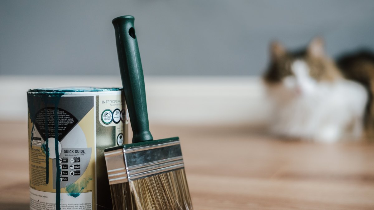 Paint brush resting near a paint can on parquet flooring indoors.